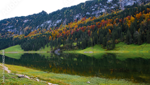 Surrounded by majestic mountains, the tranquil waters of Falensee mirror the stunning autumn foliage, creating a picturesque moment in Appenzell, where nature's beauty flourishes. photo