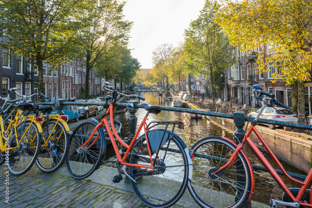 Colorful bicycles rest against the canal's edge as golden autumn leaves flutter in the breeze. The tranquil waterways of Amsterdam reflect the beautiful fall scenery, inviting exploration. Colorful bicycles rest against the canal's edge as golden autumn leaves flutter in the breeze. The tranquil waterways of Amsterdam reflect the beautiful fall scenery, inviting exploration.