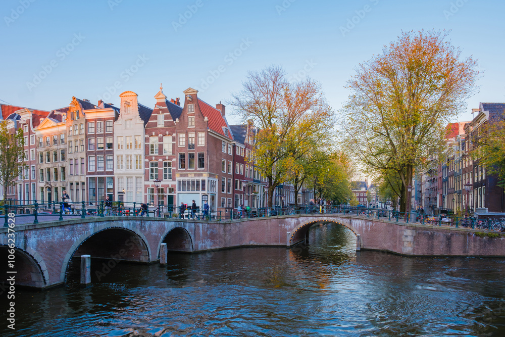 Obraz premium As autumn unfolds, vibrant leaves dance over Amsterdam Keizersgracht iconic canals. The historic architecture stands against the clear sky, inviting leisurely strolls along the tree-lined pathways.