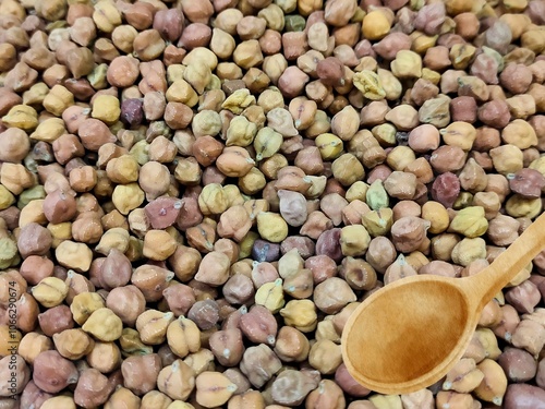 Raw, dried chickpeas, small and brown, stand out when arranged in a rustic wooden scoop. Their earthy tones and unique shapes highlight the artisanal quality of natural ingredients.
