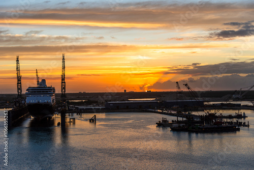 The rising sun casts a warm, golden glow over Freeport, Bahamas, illuminating the coastline and repair shipyard at the horizon. 