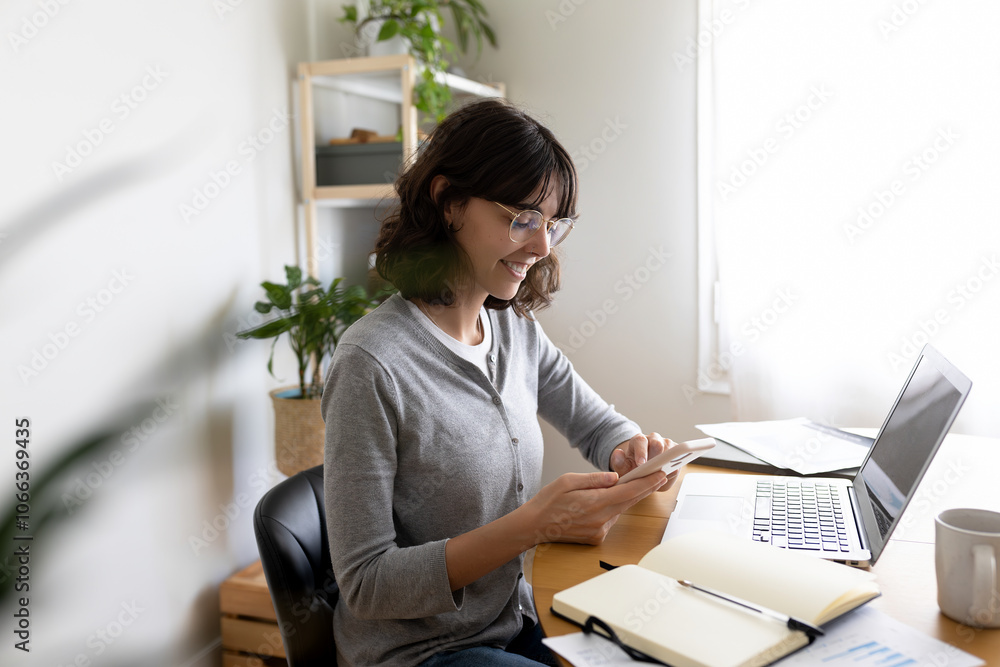 Side view of happy woman using smart phone at home office while working using laptop. Copy space. Side view of happy woman using smart phone at home office while working using laptop. Copy space.