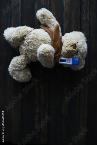 Stuffed Teddy Bear Holding Thermometer on Dark Wooden Background