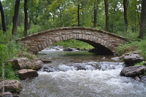 Stone arch bridge spanning a flowing creek in lush green forest