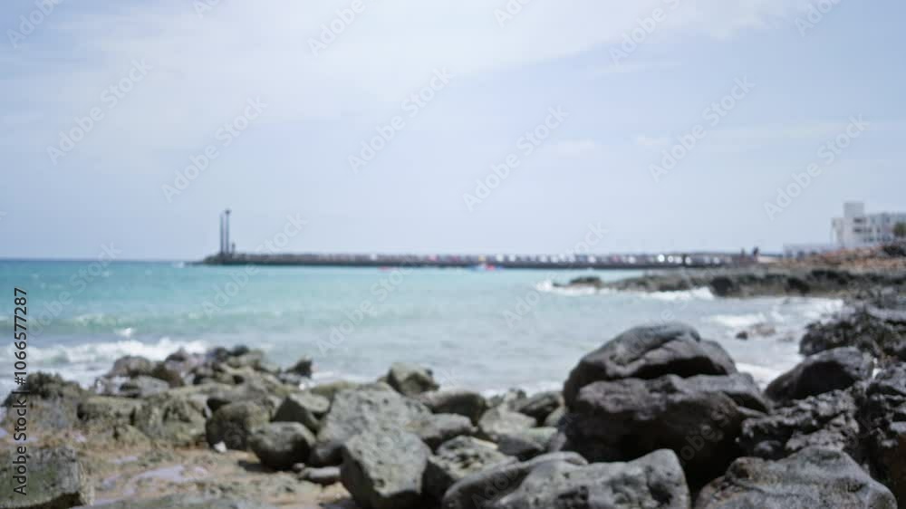 Blurred view of rocky beach coastline in lanzarote, canary islands, spain, with distant pier and buildings in background. Blurred view of rocky beach coastline in lanzarote, canary islands, spain, with distant pier and buildings in background.