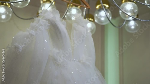 A stunning white wedding dress is showcased in a modern room with a glamorous chandelier and elegant decor, ideal for a bridetobe looking for sophistication and luxury for her special day photo