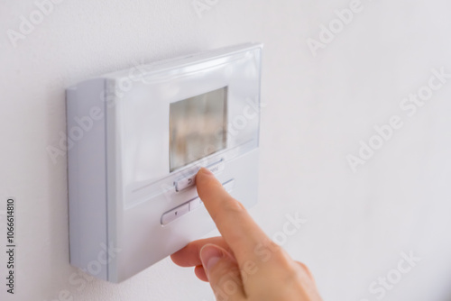 Hand adjusting digital thermostat on wall to control room temperature