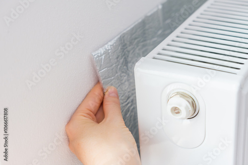 Hand installing thermal insulation behind radiator to reflect heat into the room