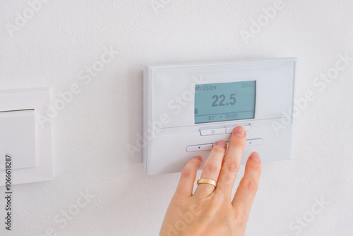 Hand adjusting digital thermostat on wall to control room temperature