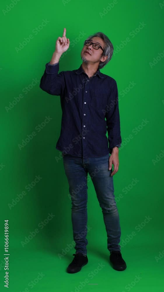 A vertical shot of a senior Asian man standing against a green background. A vertical shot of a senior Asian man standing against a green background.