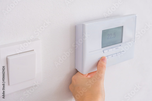 Hand adjusting digital thermostat on wall to control room temperature