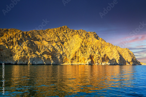 Golden hour at Khasab Fjord in Oman’s Musandam Peninsula, where calm waters mirror the rugged cliffs at sunset