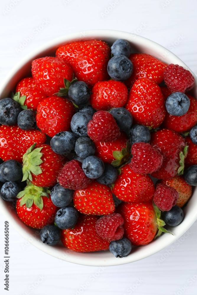 Different fresh ripe berries in bowl on wooden table, top view Different fresh ripe berries in bowl on wooden table, top view
