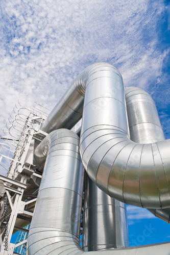 In the photo there is a pipeline and a metal ladder, in the background there is a blue sky and clouds