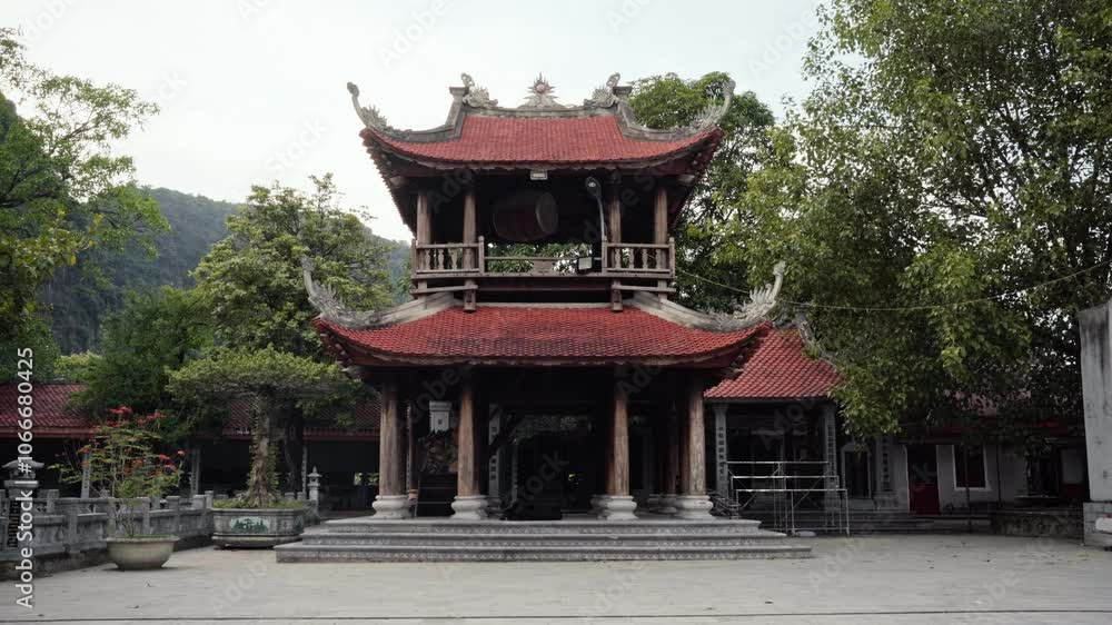 Fixed shot of a traditional Vietnamese temple pavilion in Tam Coc Vietnam The building features curved red-tiled roofs, intricate dragon carvings, and a drum in the upper level lush greenery mountains Fixed shot of a traditional Vietnamese temple pavilion in Tam Coc Vietnam The building features curved red-tiled roofs, intricate dragon carvings, and a drum in the upper level lush greenery mountains