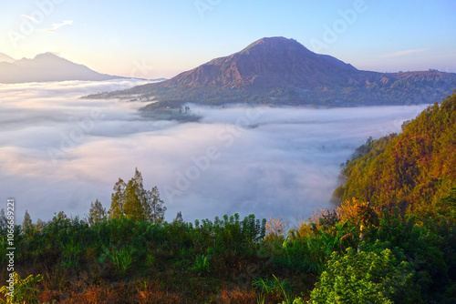 Sunrise view with fog and warm sunlight over the Bali mountains. Majestic nature landscape background of Mount Batur from Desa Pinggan, Kintaman, Bali, Indonesia. photo