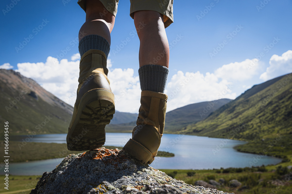 Hiker legs wearing leather boots hiking on high altitude mountain top,with a lake in the distance Hiker legs wearing leather boots hiking on high altitude mountain top,with a lake in the distance