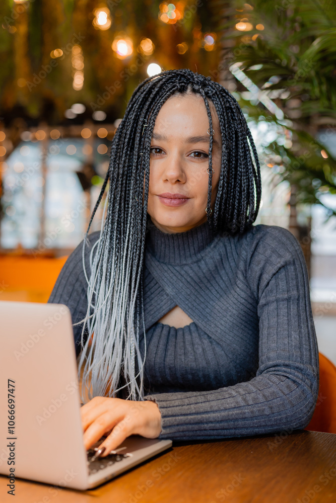 young woman with Afro braids is sitting in a coffee shop and working on a laptop young woman with Afro braids is sitting in a coffee shop and working on a laptop