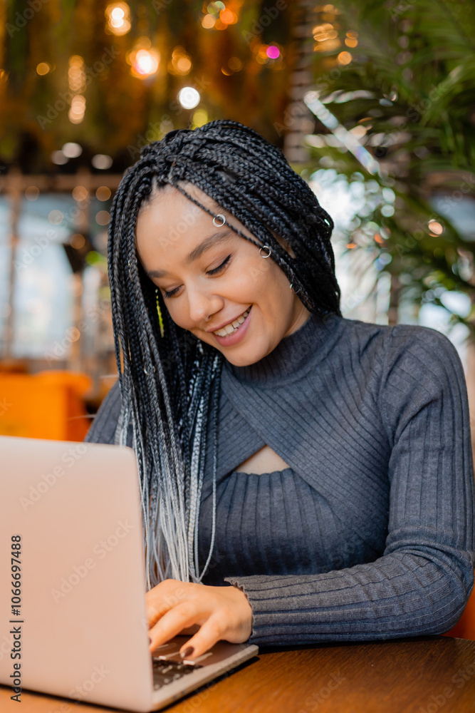 young woman with Afro braids is sitting in a coffee shop and working on a laptop young woman with Afro braids is sitting in a coffee shop and working on a laptop