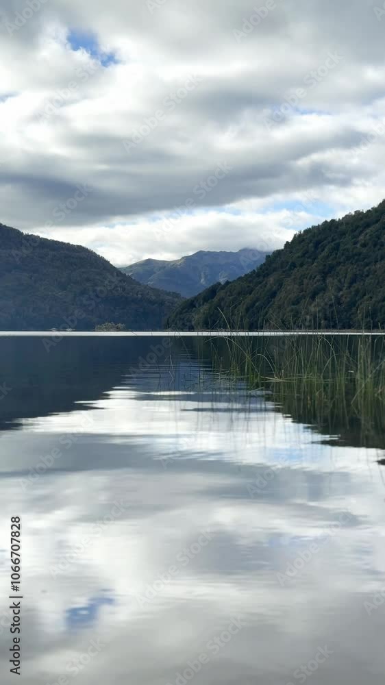 A lake with a cloudy sky in the background. The water is calm and still. The reflection of the sky and mountains can be seen in the water A lake with a cloudy sky in the background. The water is calm and still. The reflection of the sky and mountains can be seen in the water