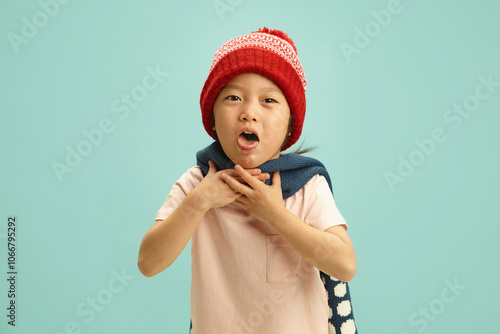 Sick Chinese apperance child with a ill throat having acute coughing attack, wearing in winter hat, woolen scarf is wrapped around her neck, difficult for her to breathe, she clutches at her throat photo