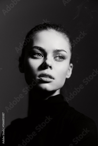 Pensive young woman with a sleek ponytail, wearing a black turtleneck, gazing thoughtfully into the distance against a dark backdrop. Emotional portrait concept.