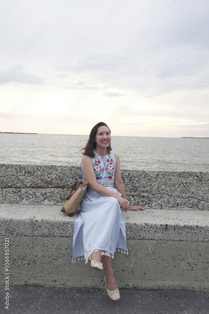 Asian female tourist vacationing on vacation wearing a dress and sitting on a beach chair watching the sunset at sea