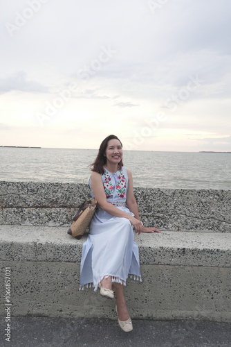 Obraz na płótnie Asian female tourist vacationing on vacation wearing a dress and sitting on a beach chair watching the sunset at sea w salonie
