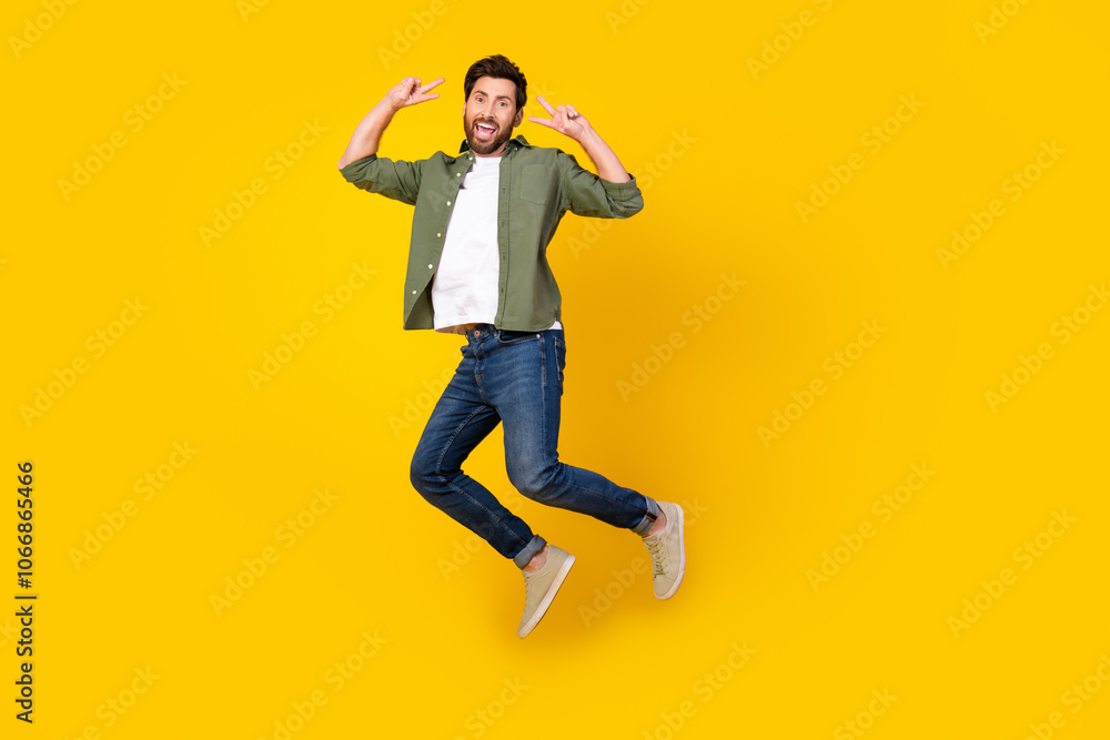 Full length portrait of nice young man jump show v-sign wear shirt isolated on yellow color background Full length portrait of nice young man jump show v-sign wear shirt isolated on yellow color background