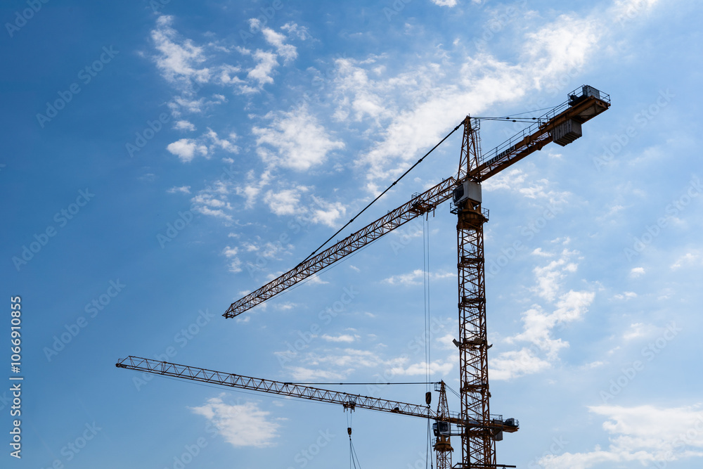 Silhouette of Construction Cranes Set Against a Bright Blue Sky During Daytime Hours