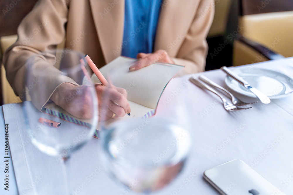 Close-up of a woman holding a pen, writing in a notepad, working in a cafe. Business woman hand writing with pen in notepad at cafe.