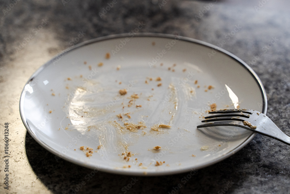 Dirty white ceramic plate with leftovers of food and fork, top view