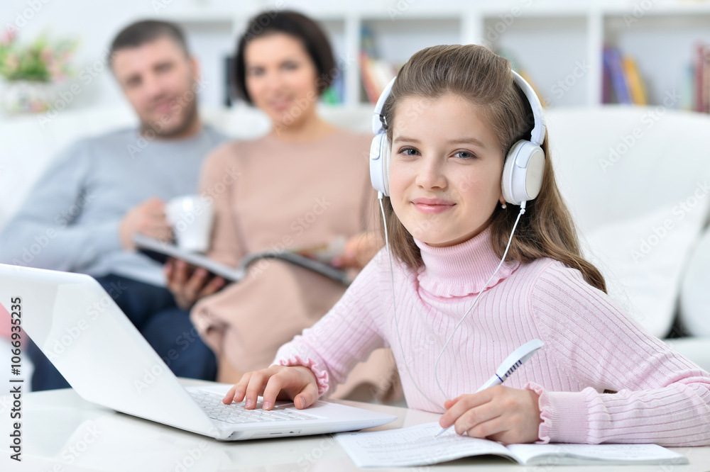 Cheerful little girl using a laptop at home with her parents in the background. Cheerful little girl using a laptop at home with her parents in the background.