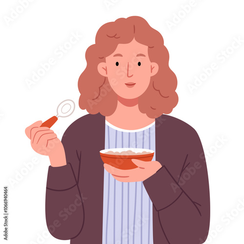 A red-haired girl in a brown cardigan eats oatmeal from a red plate and holds a spoon in her hand.The girl is eating.