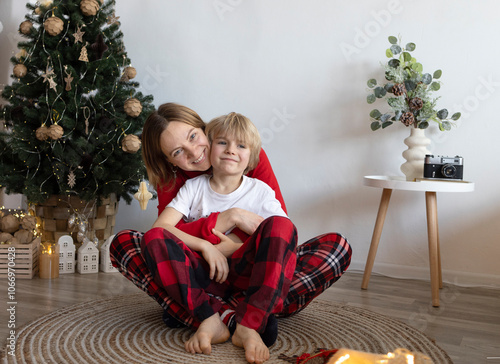 Mom and son sit cuddling next to each other in a room decorated for Christmas. Christmas Eve with family. A cozy home on winter weekends and holidays. positive attitude for the new year