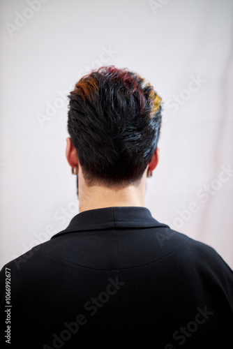 man in black shirt and dark hair with light highlights, standing on white background. stylish men's model hairstyle, back view