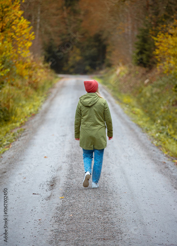 middle-aged caucasian woman in hat and jacket is walking by trail in the autumn forest 