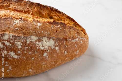 This image showcases a freshly baked, crispy golden bread loaf on a pristine marble kitchen surface, highlighting the texture and artisanal quality of the bread. photo