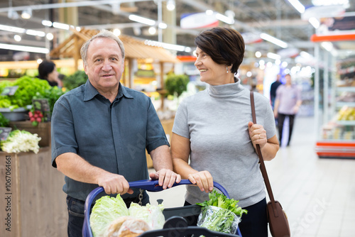 Photos Mature couple standing in grocery store with groceries in cart