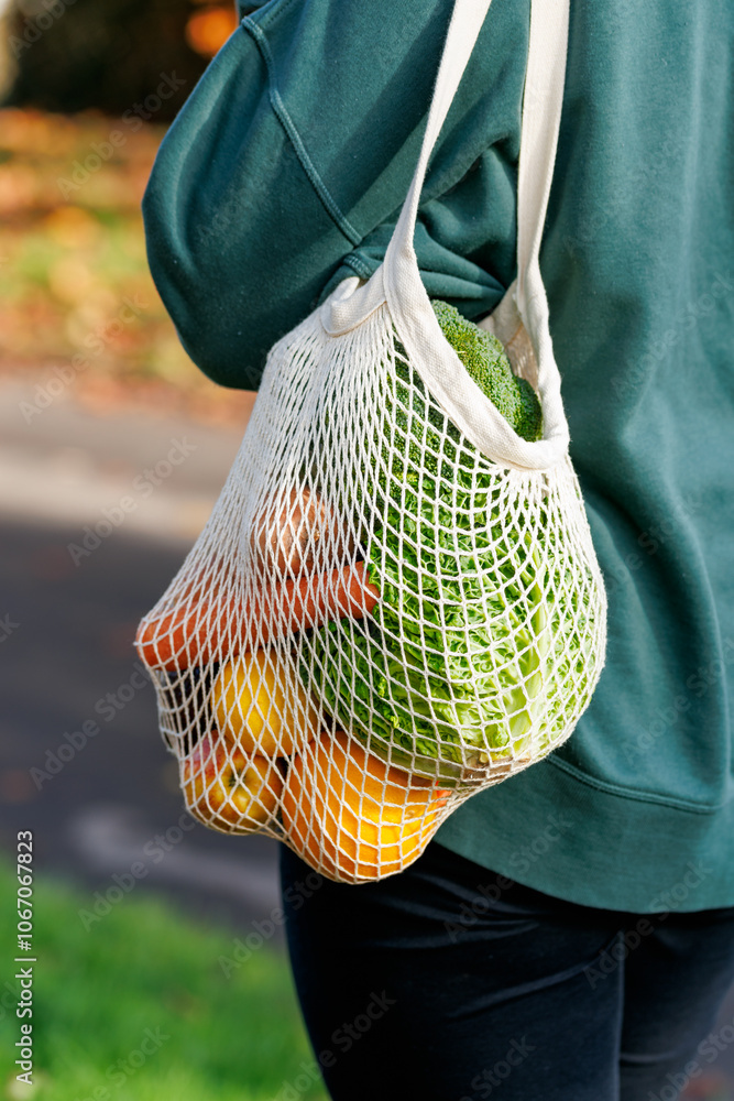 Woman Holding reusable Mesh grocery shopping Bag with Fresh Vegetables and fruits. Eco-friendly bag filled with fresh produce held by a person