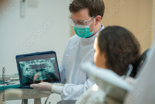 The dentist shows the results of the x-ray film to the patient's teeth on a tablet. The patient received a result, consultation, and discussed the plan to cure her oral.
