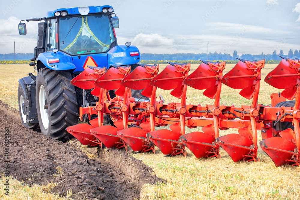 A blue tractor plowing a vast field under a bright sky in the countryside