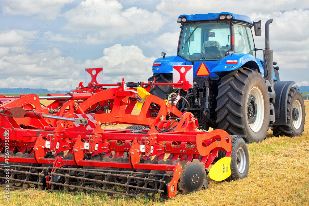 Vibrant blue tractor preparing farmland with red tillage equipment under a sunny sky Vibrant blue tractor preparing farmland with red tillage equipment under a sunny sky