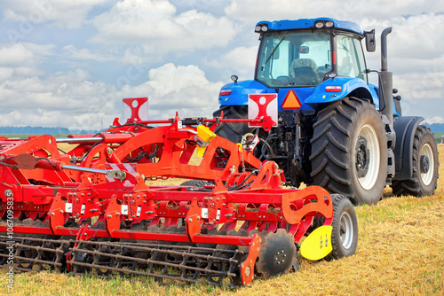 Obraz na płótnie Vibrant blue tractor preparing farmland with red tillage equipment under a sunny sky w salonie