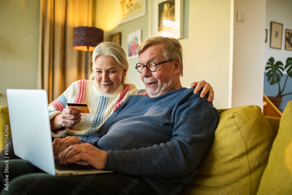 Senior couple online shopping on laptop on the couch at home Senior couple online shopping on laptop on the couch at home