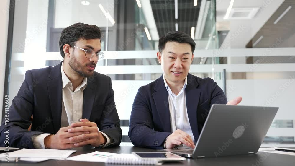 Two businessmen celebrate success at work using laptop. Colleagues read the good news on the computer. Expressing excitement, teamwork, and achievement sitting at desk at workplace in business office Two businessmen celebrate success at work using laptop. Colleagues read the good news on the computer. Expressing excitement, teamwork, and achievement sitting at desk at workplace in business office
