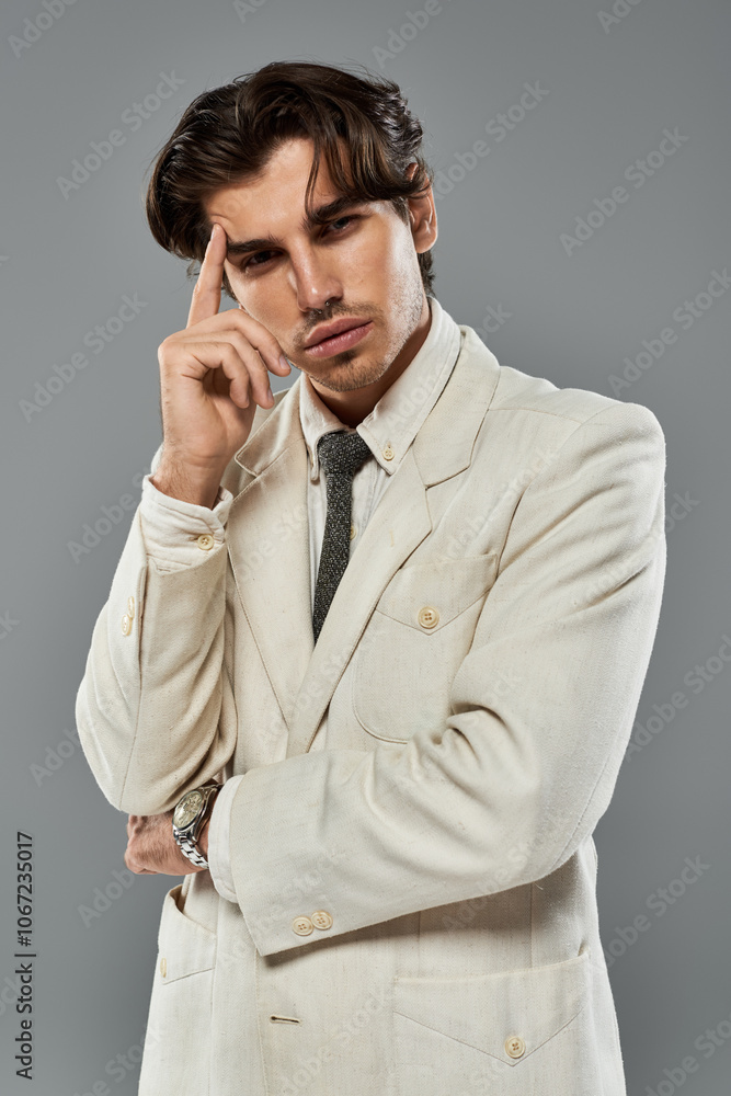 A handsome young man in elegant formal wear thoughtfully poses in a studio with a grey background. A handsome young man in elegant formal wear thoughtfully poses in a studio with a grey background.
