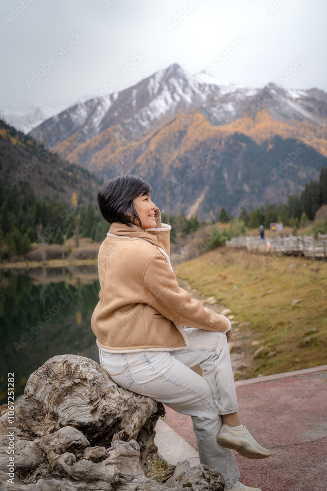 Fototapeta premium Happy travel girl sitting by the mountain lake and looking at view in autumn at Dagu Glacier Park , China.People with landscape concept.