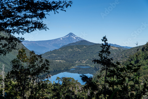 Obraz na płótnie A scenic view from Huerquehue National Park in southern Chile, showcasing a tranquil lake and distant volcano surrounded by lush, dense forest, capturing the natural beauty of the landscape. w salonie