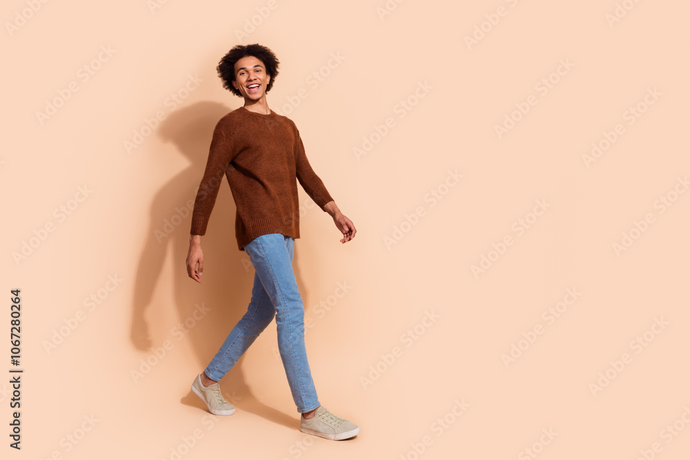 Fototapeta premium Cheerful young African American man walking confidently in casual outfit against a beige background